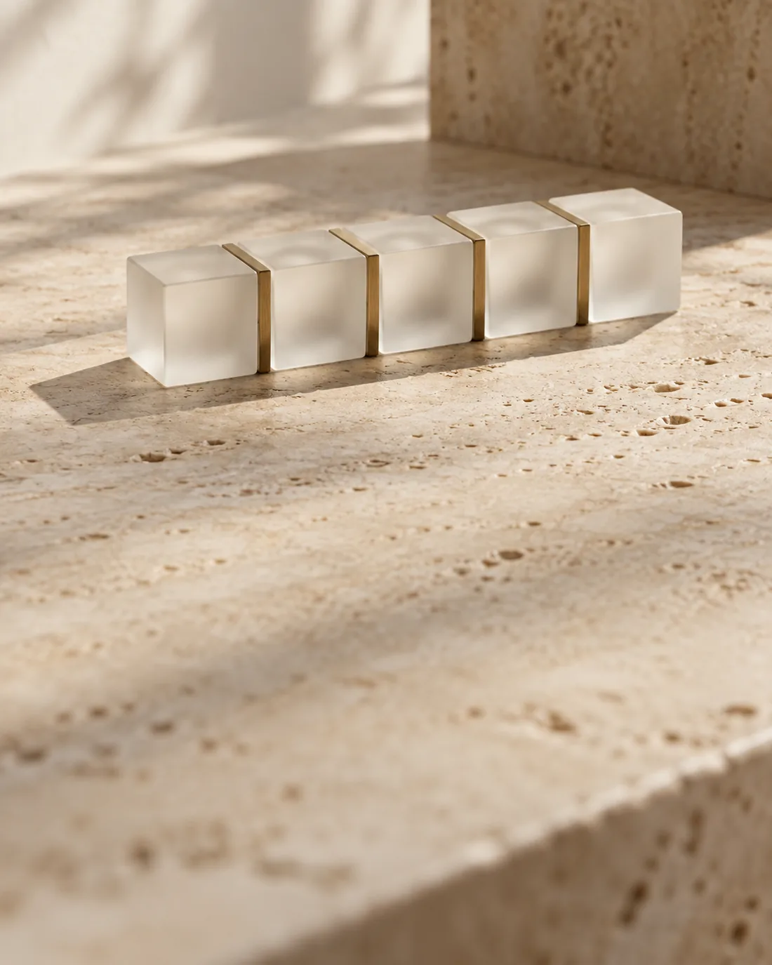 Still life: a chain of frosted glass cubes joined by brass seams on travertine, a metaphor for a ledger.