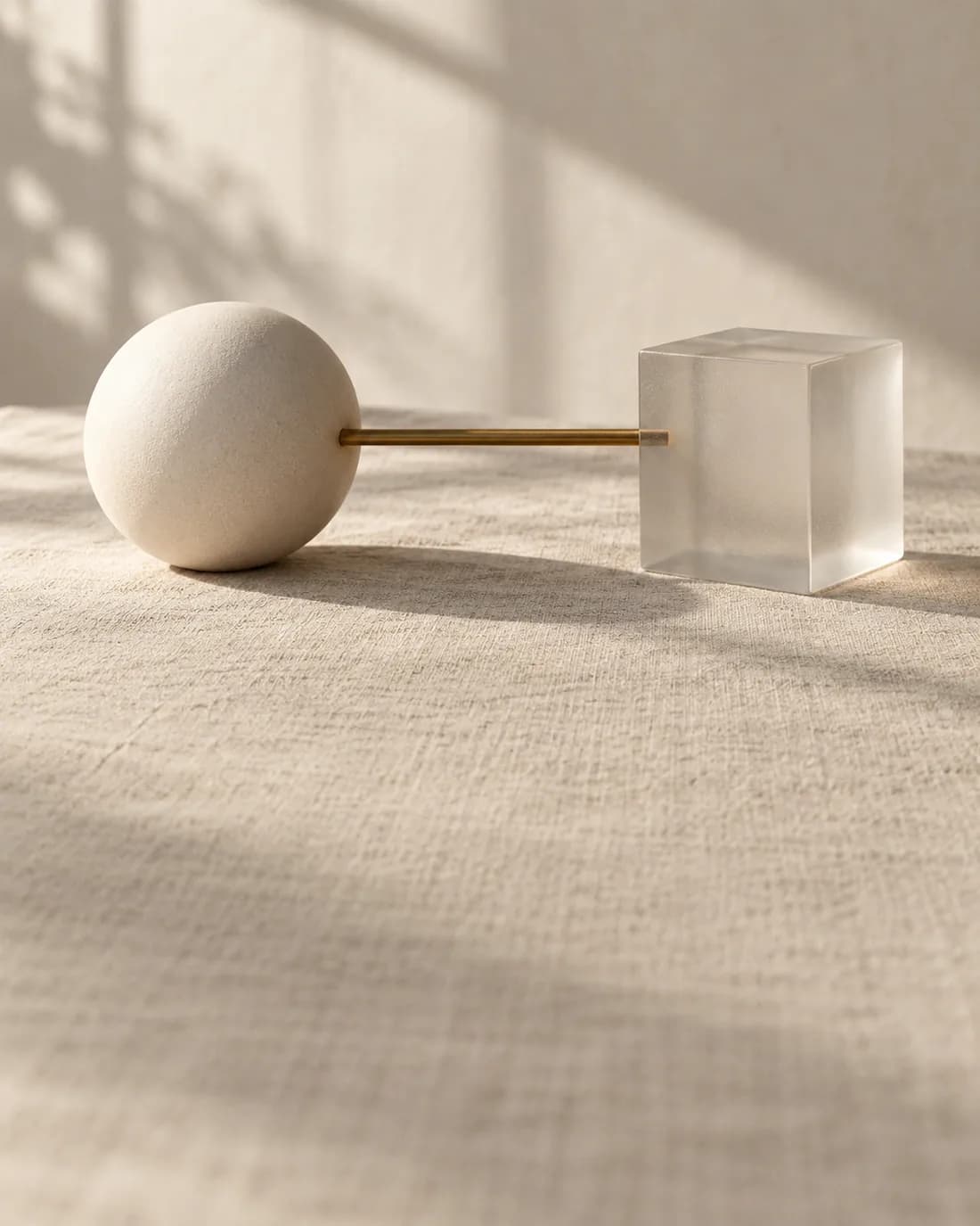 Still life: an ivory sphere and a frosted glass cube joined by a slender brass rod, a metaphor for AI bridged to blockchain.